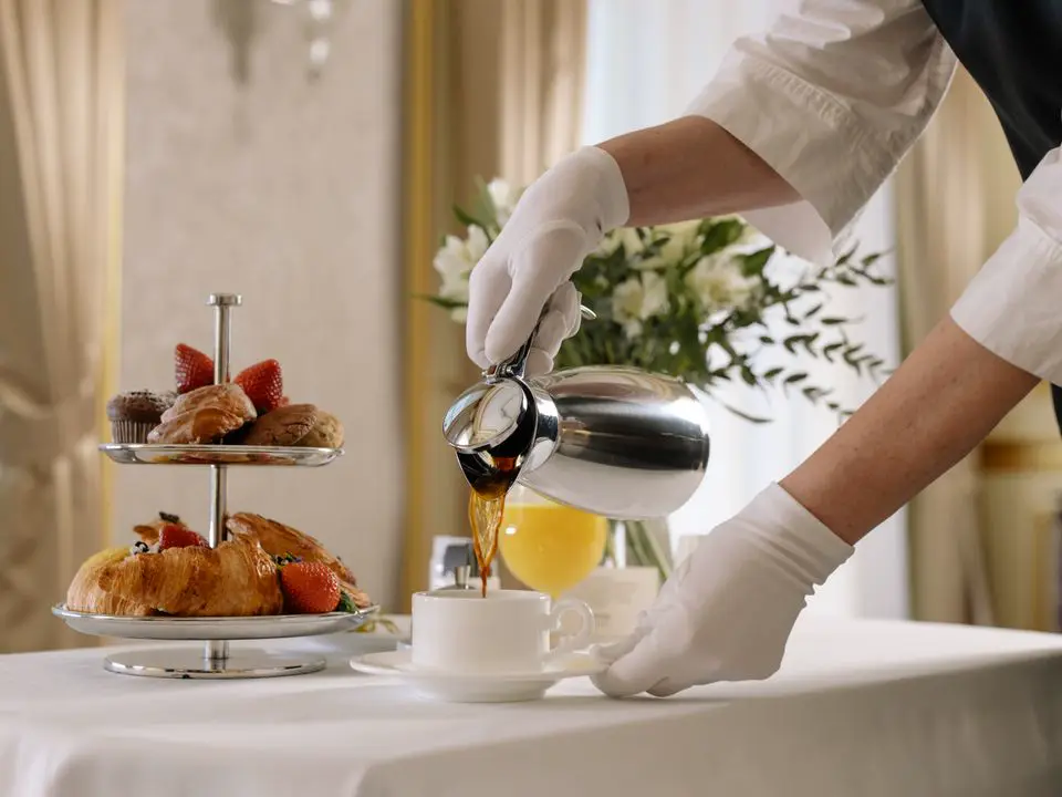 Konobar u bijelim rukavicama sipa kafu uz hotelski doručak s kroasanima