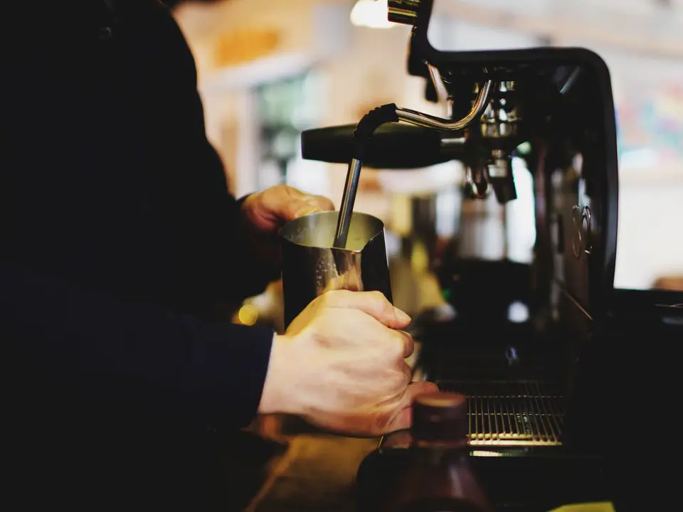 Barista toči kafu iz aparata za espresso u lokalu s toplim svjetlom